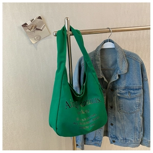 Detail of green canvas tote bag with black letter print hanging next to denim jacket