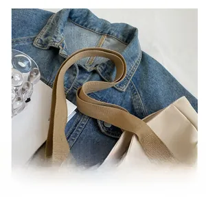 Detail of canvas tote bag featuring durable wide brown shoulder strap on denim background