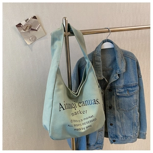 Detail of mint green canvas hobo bag with black text print hanging on metal rack