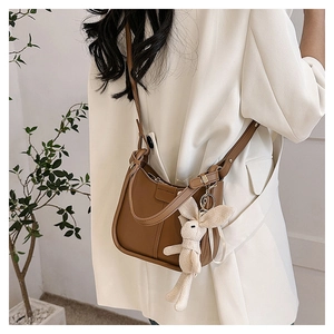 Brown leather crossbody bag detail with cute white knitted rabbit charm and adjustable strap