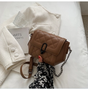 Détail d'un sac bandoulière marron matelassé avec boucle ovale noire mate et chaîne