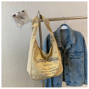 Close-up of beige canvas tote bag with printed text hanging against a denim jacket