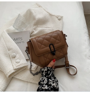 Détail d'un sac bandoulière marron matelassé avec chaîne en métal et boucle en U