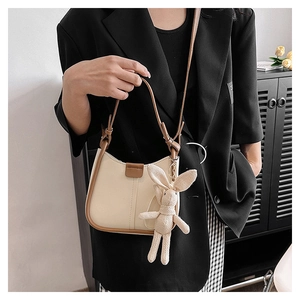 Detail of cream shoulder bag with brown trim and cute beige knit rabbit charm accessory