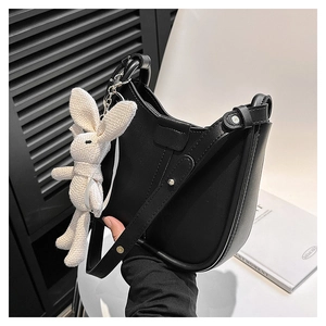 Detail of a black leather crescent shoulder bag with a cute plush rabbit pendant charm