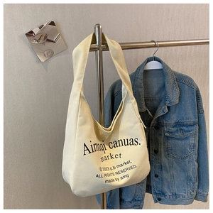 Detail of off-white canvas tote bag with black text hanging on a metal hanger