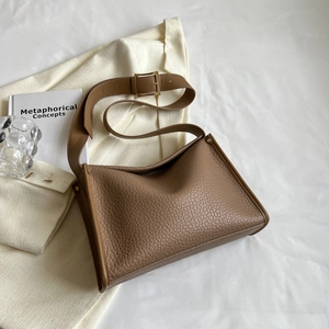 Borsa tote in pelle marrone con ampia tracolla in un contesto urbano minimalista