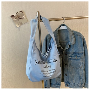 Detail view of light blue canvas tote bag hanging on a rack with black typography