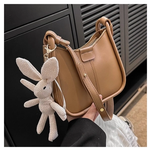 Brown leather shoulder bag with sleek curved top and cute white rabbit pendant detail