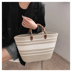 Detail of woven tote bag featuring natural bamboo handles and textured striped pattern