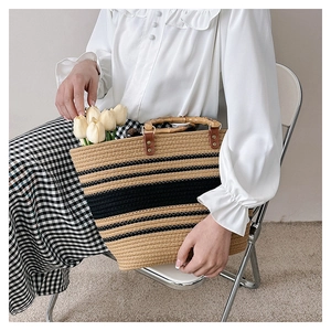 Detail of woven straw tote bag featuring chic bamboo handles and black stripe accents
