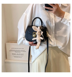 Detail of black pebbled leather mini saddle bag with golden clasp and cute rabbit pendant