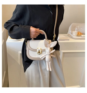 Detail of cream saddle bag featuring gold clasp and cute knit bunny charm accessory