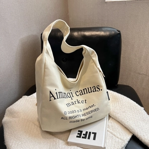 Minimalist beige canvas tote bag with black print displayed on a stylish leather seat