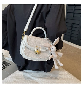 Detail of cream saddle bag featuring lychee texture and a knit rabbit pendant