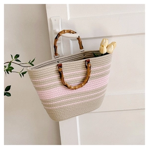 Detail of woven tote bag with bamboo handles and pink stripes hanging on a white door
