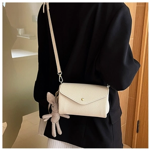 Detail of cream envelope crossbody bag with gold buckle and plush rabbit keychain charm