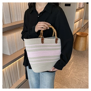 Detail of woven tote bag featuring bamboo handles and pink striped cotton rope texture