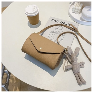Close-up of khaki litchi grain leather crossbody bag with cute bunny charm on a table