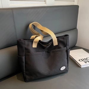 Minimalist black canvas tote bag with khaki straps and large front pockets