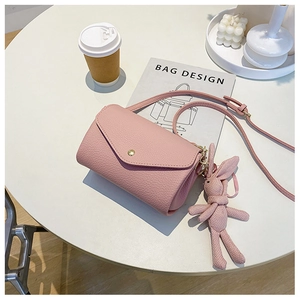 Pink lychee leather crossbody bag with envelope flap and cute rabbit charm on white table