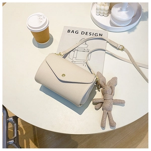 Beige pebble leather crossbody bag with triangular flap and cute bunny charm on table