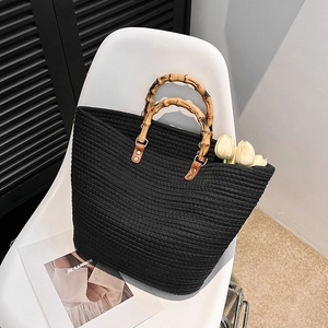 Black woven tote bag with bamboo handles and spacious design on a minimalist background
