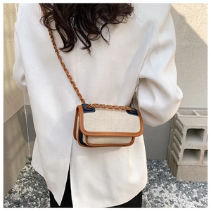 Detail of canvas shoulder bag with brown leather trim and woven chain strap on a model