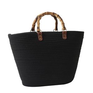 Woven black tote bag featuring natural bamboo handles and premium leather stitching detail