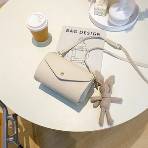 Off-white pebble grain square crossbody bag with rabbit charm on a minimalist desk