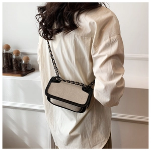 Detail of woven crossbody bag with black leather trim and elegant chain strap on shoulder
