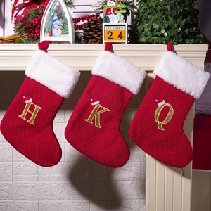 Three red knitted Christmas stockings with gold initial embroidery hanging on fireplace