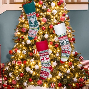 Three-piece knitted Christmas stockings with reindeer and trees hanging on a festive tree