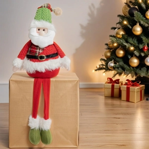 Charming long-legged Santa plush doll sitting on a gift box near a lit Christmas tree