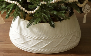 Detalle del cubre pie de árbol de Navidad en punto trenzado crema sobre suelo madera