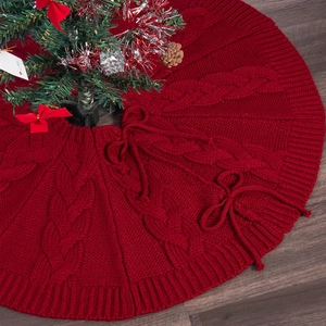 Macro shot of red cable knit Christmas tree skirt with decorative bow on wood floor