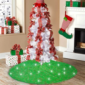 Close-up of green round Christmas tree skirt with spiral patterns and glowing LED lights