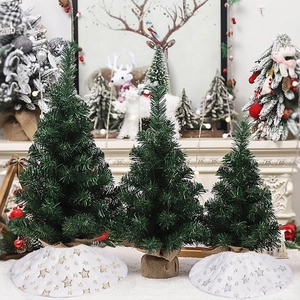 Three sizes of artificial Christmas trees with burlap bases in a cozy home fireplace setting
