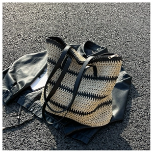 Detail of woven straw tote bag featuring black stripes, leather straps and a top zipper