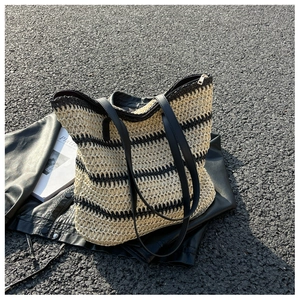 Top view of striped straw tote bag with black leather straps on a biker jacket background