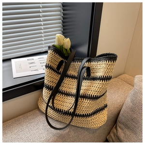Detail of woven straw tote bag with black stripes and leather straps in a bright room