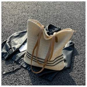 Detail of straw tote bag with black stripes and brown leather straps on a textured surface