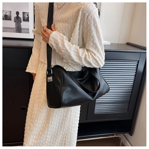Side view of a large black textured leather pillow bag worn as a shoulder bag