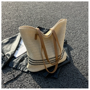 Detail of woven straw tote bag with black stripes and brown leather shoulder straps