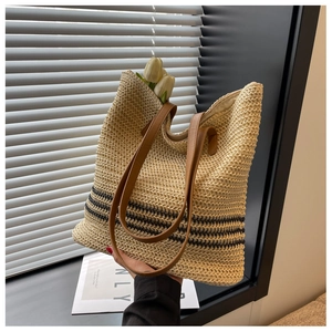 Detail of hand-held straw tote bag with black stripes and brown leather straps