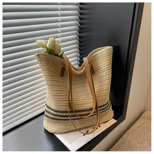 Detail of woven straw tote bag with black stripes and brown leather handles in soft sunlight