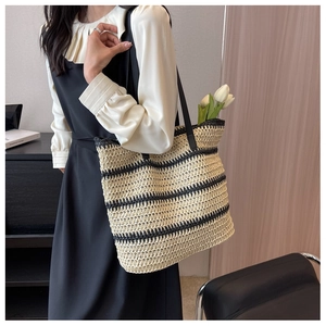 Close-up of a large striped straw tote bag with black leather straps on a shoulder