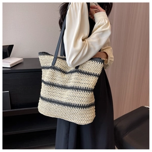 Close-up of a striped straw tote bag with black straps and golden zipper closure