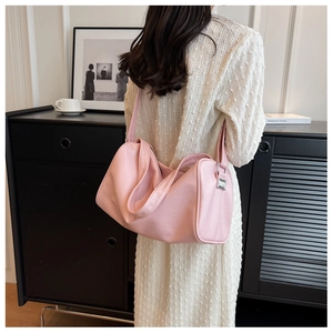 Close-up of pink lychee textured cylinder bag worn as a shoulder bag in a stylish room