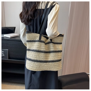 Model wearing large black and white striped woven straw tote bag with black leather straps